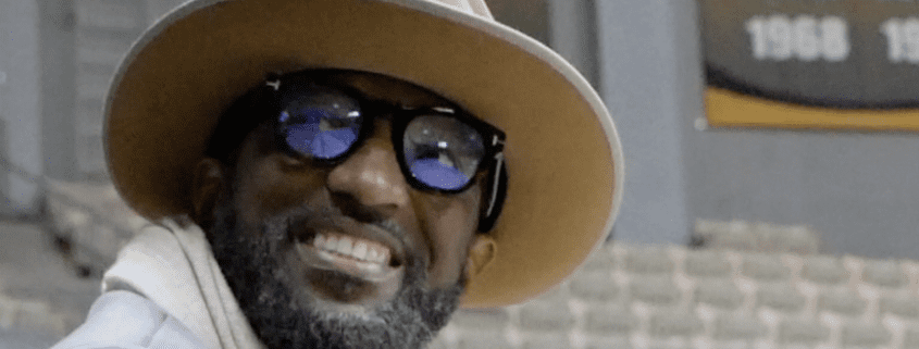 Man smiling, wearing hat and sunglasses indoors.